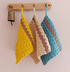 3 crochet cloths hanging on a rail in yellow and blue