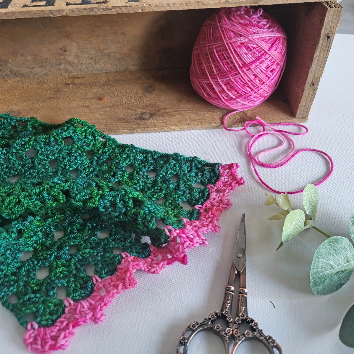 a green lace scarf and a ball of pink yarn on a desk