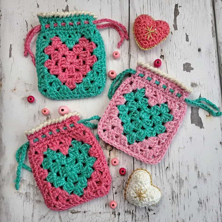 3 crochet heart bags and small stuffed crochet hearts on a white board