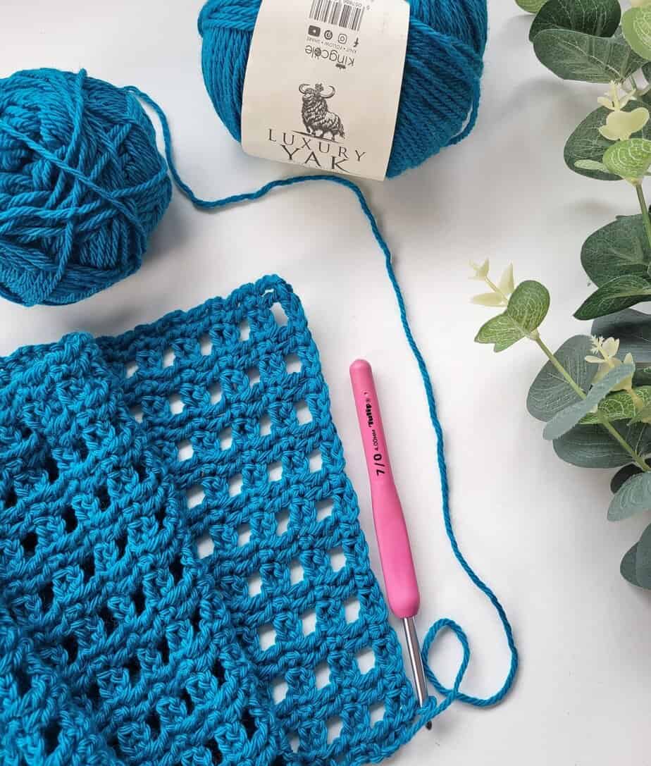 crochet filet scarf and yarn and a pink crochet hook on a white background