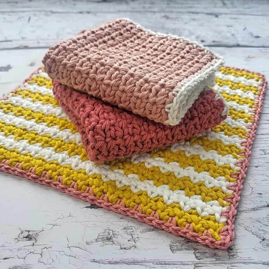 3 crochet dishcloths with 2 folded on a yellow and cream cloth