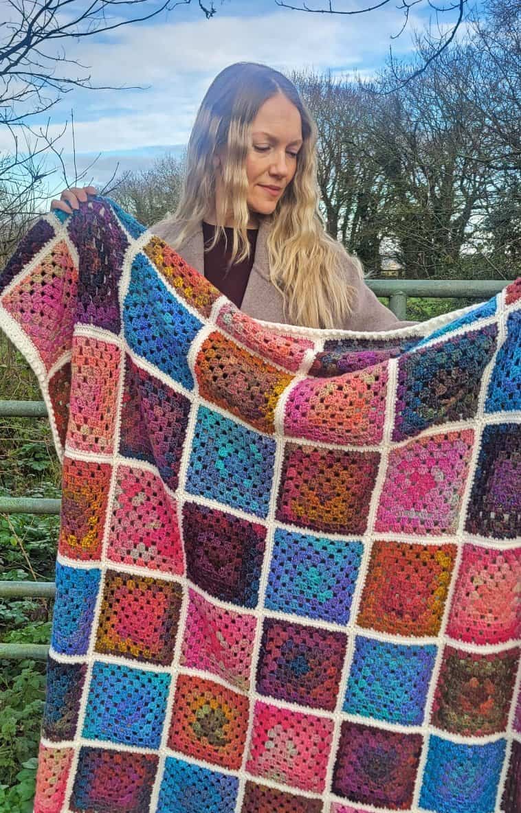 Granny square blanket made with variegated yarn, held up to show the scale of the finished item