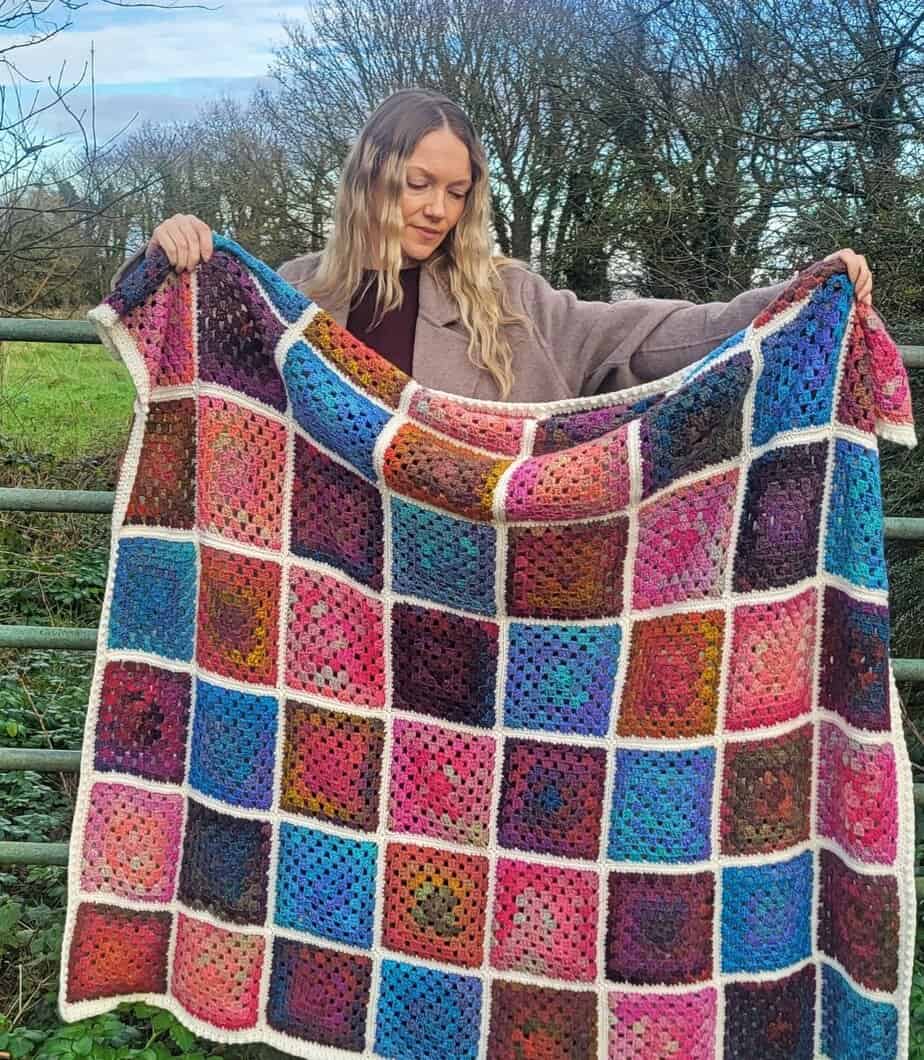 Granny square blanket made with variegated yarn, held up to show the full blanket