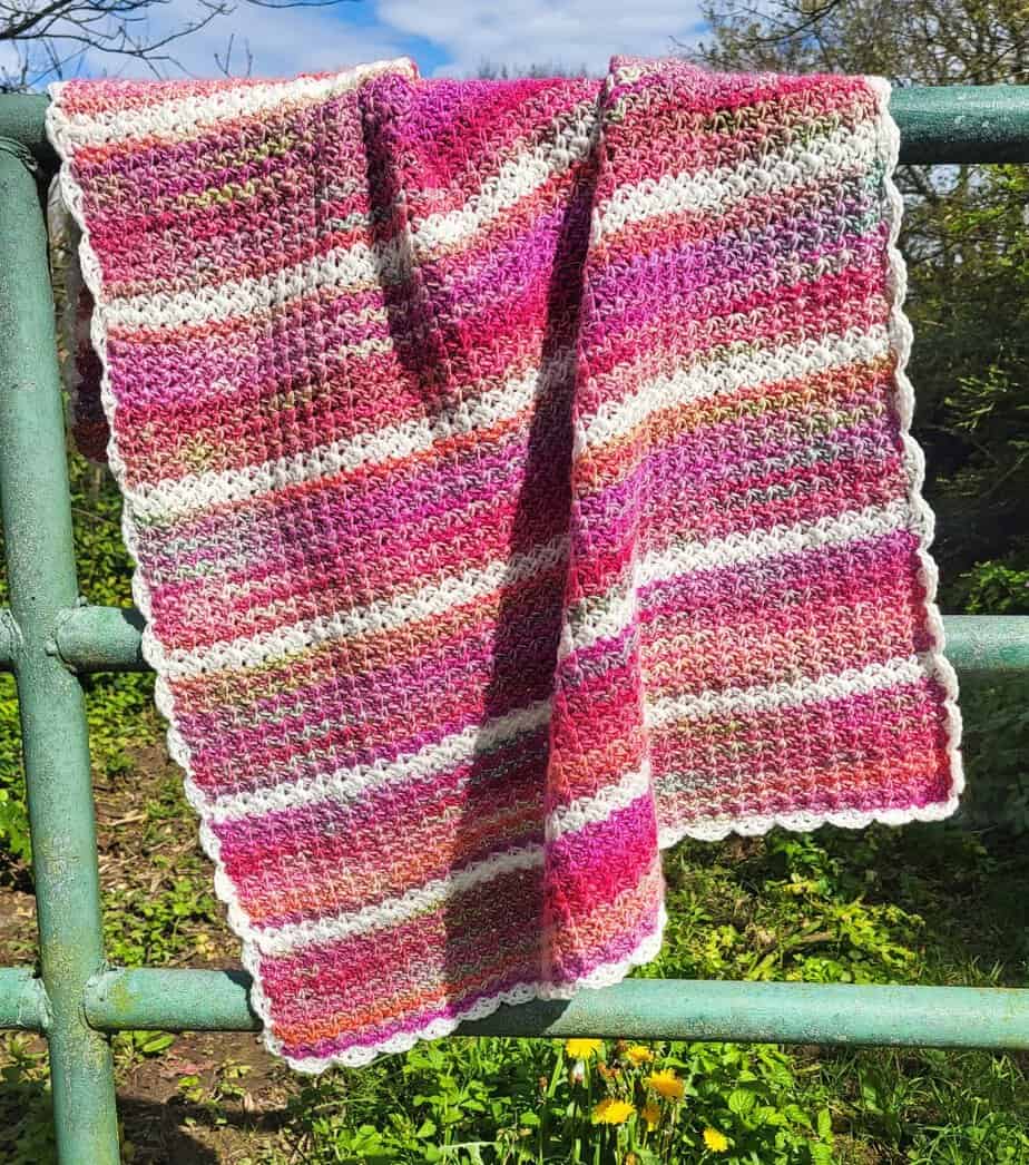 Another view of the Pink Drift baby blanket, displayed outside, hanging over a metal fence