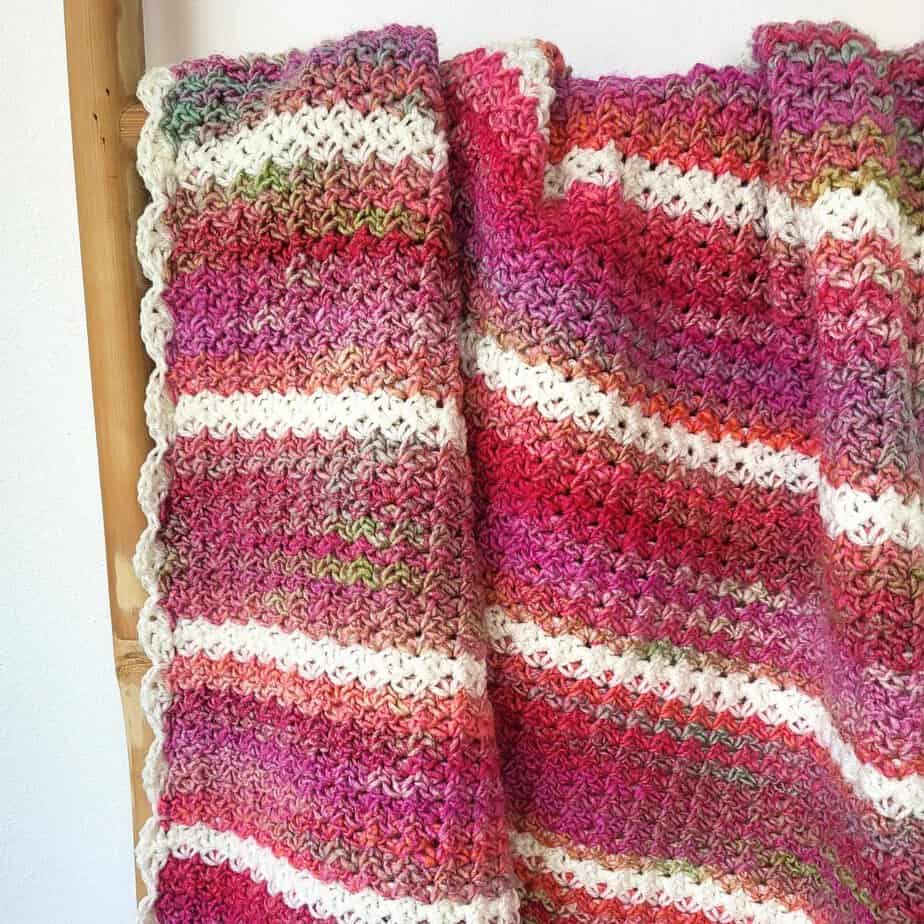 Close-up photo of Pink Drift, a one row repeat crochet baby blanket, displayed on a bamboo ladder
