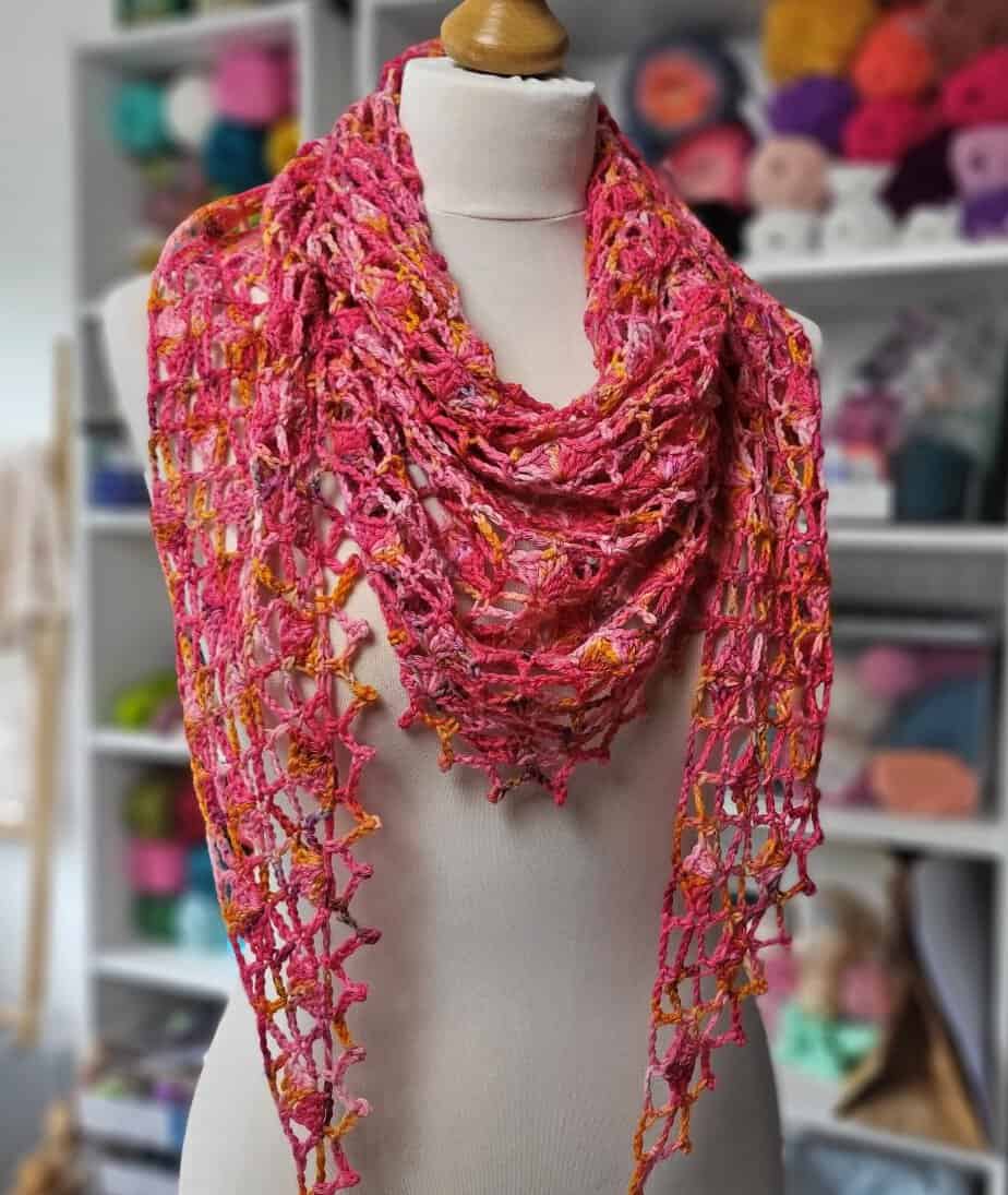 The Rosehip shawl displayed on a mannequin, with shelves of yarn in the background