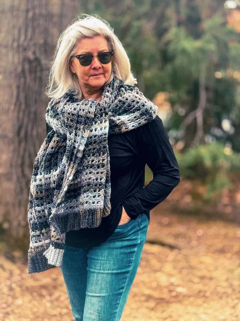 big crochet scarf on a woman standing by a tree