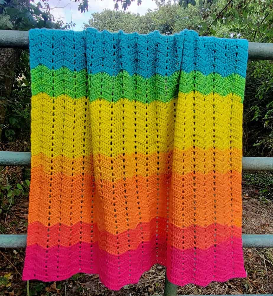 Double Crochet Ripple Blanket hanging on a metal fence