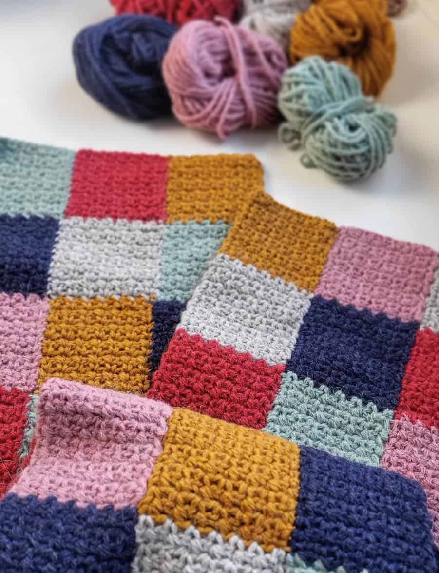 closeup of the patchwork crochet scarf with balls of yarn