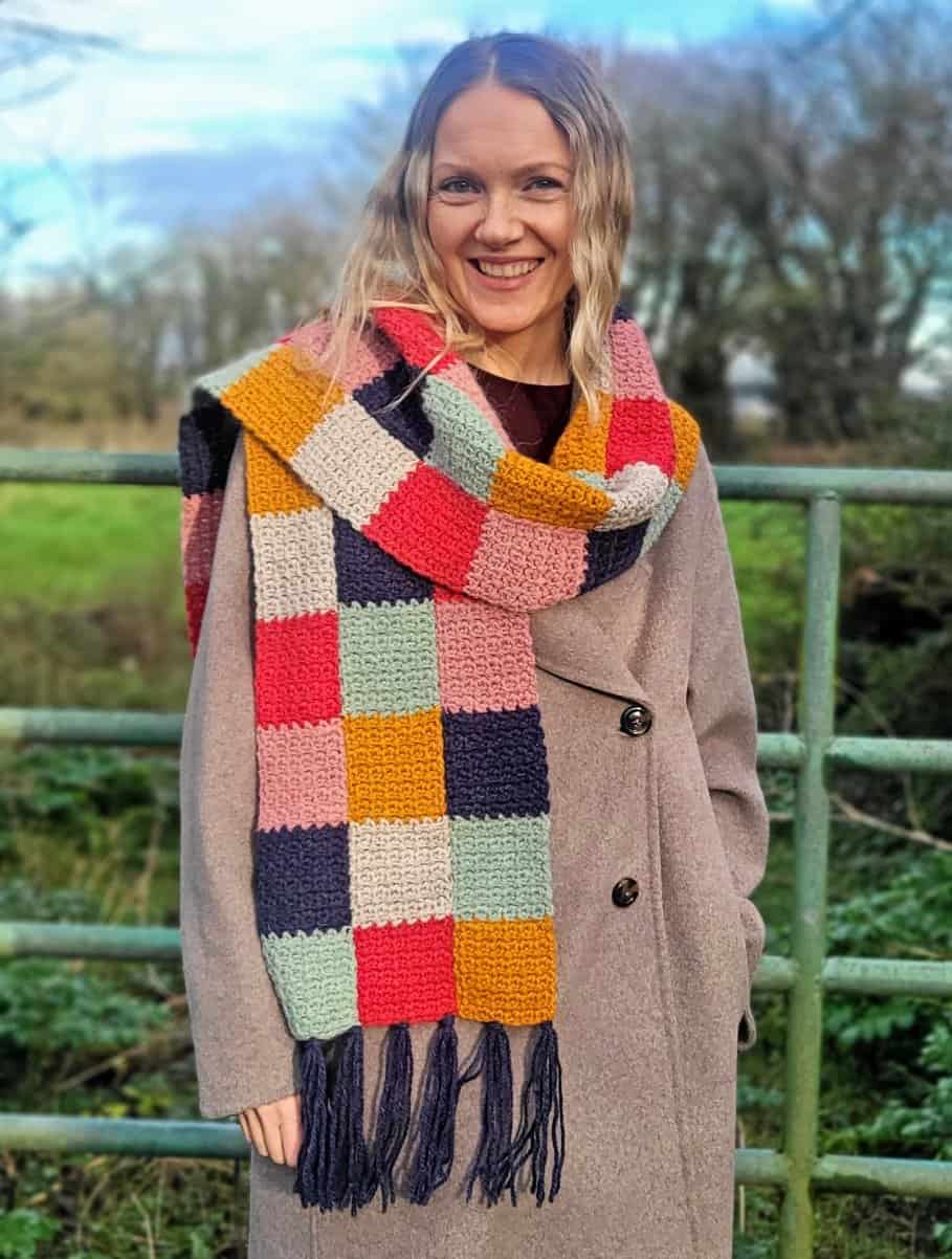 a smiling woman wearing a colorful patchwork crochet scarf